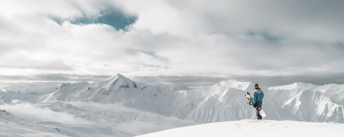 Snowboarder steht oben am Berg und blickt auf das Panorama