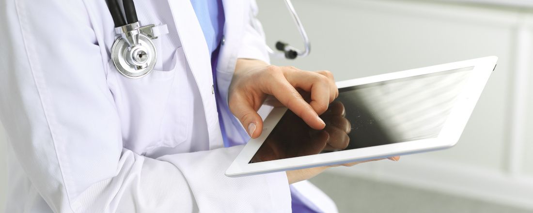 Ärztin in einem weißen Kittel und mit einem Stethoskop um den Hals hält ein Tablet in der Hand