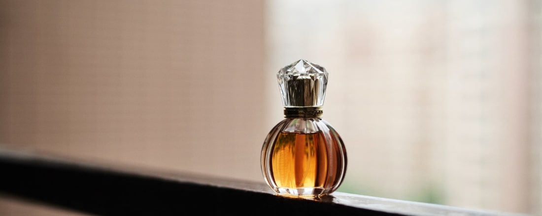 Parfumflakon mit bernsteinfarbenem Inhalt vor einem sandfarbenen Hintergrund