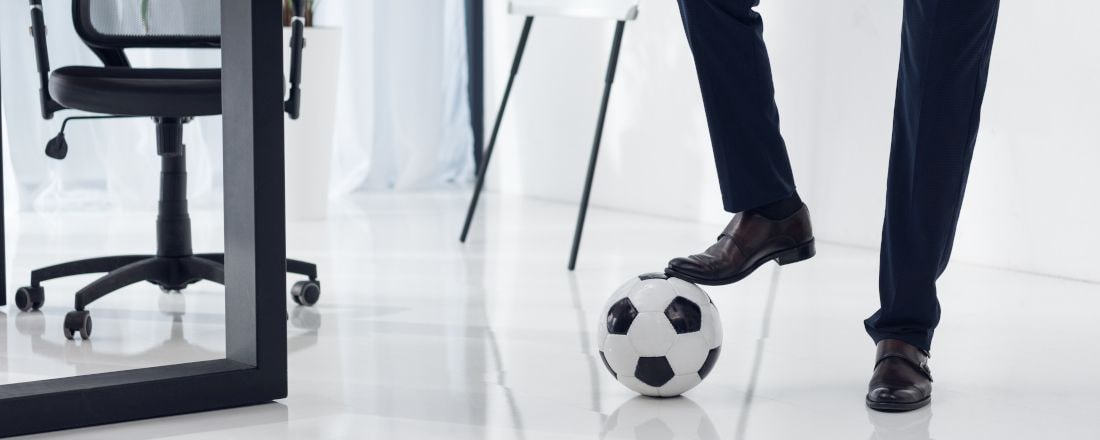 Titelbild für den berufsbegleitenden MBA Sportmanagement. Ein Manage spielt Fußball in einem modernen Office.